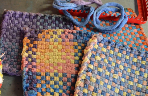 Completed woven potholders with a loom and weaving loops in the background
