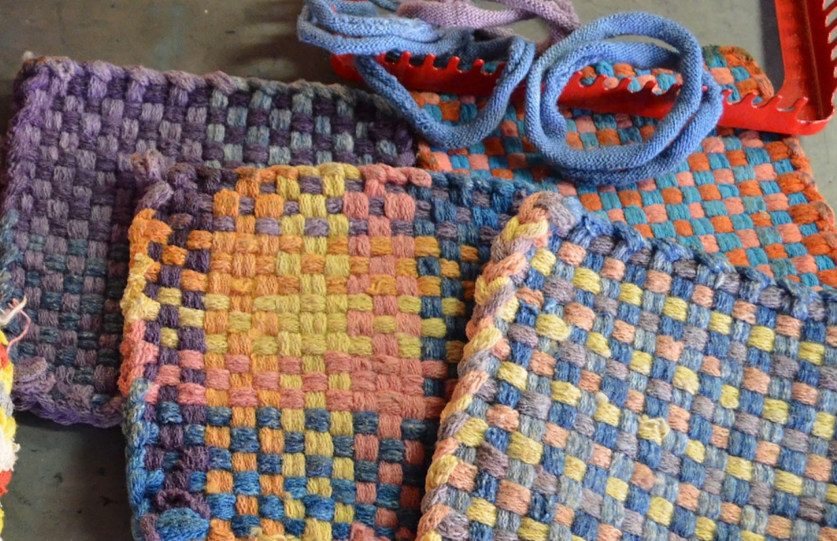 Completed woven potholders with a loom and weaving loops in the background